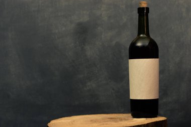 Eski bir ahşap masa üzerinde beyaz dokusal etiket ile kırmızı şarap şişesi. Güzel koyu arka plan