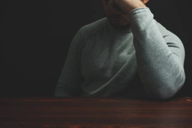 Genç adam kırmızı ahşap bir masada oturuyor. Siyah arka plan..