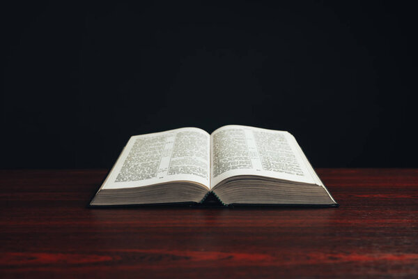 Open bible on a  red wooden table. Beautiful black background.