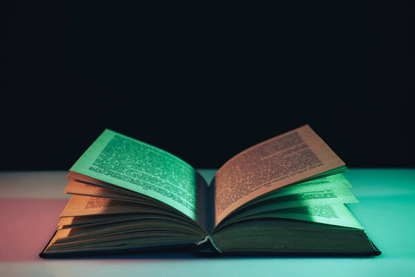 Beautiful open old book in the color light on a table and night background.