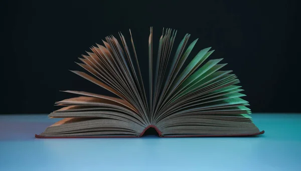 Beautiful open book pages in the color neon light on a table and night background.