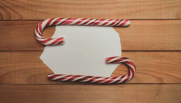 Beautiful striped hard candy cane staff on a wooden table background.