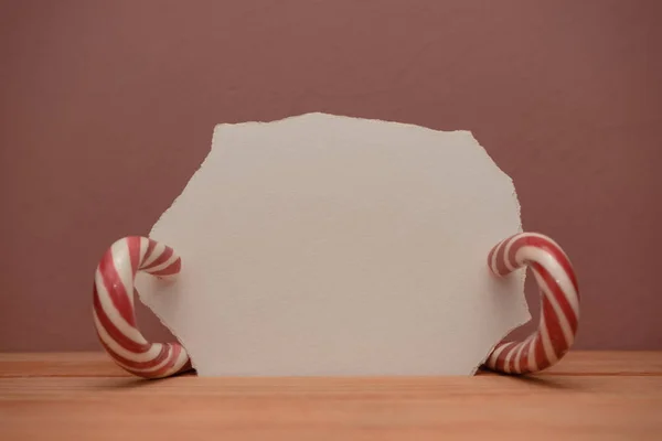 Beautiful striped hard candy cane staff on a wooden table and red wall background.