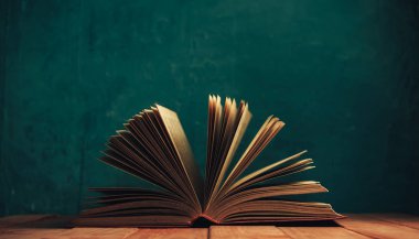 Kırmızı ahşap bir masanın üzerinde güzel, eski bir kitap. Yeşil duvar arkaplanı.