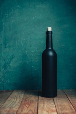 Kahverengi ahşap bir masada siyah şişe şarabı. Güzel Yeşil Duvar arkaplanı.