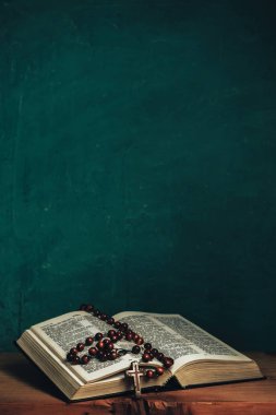 İncil 'i ve boncukları kırmızı ahşap bir masada aç. Güzel yeşil duvar arkaplanı.