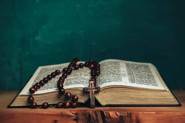 赤い古い木製のテーブルの上に聖書とビーズの十字架を開きます 美しい緑の壁の背景 — ストック写真