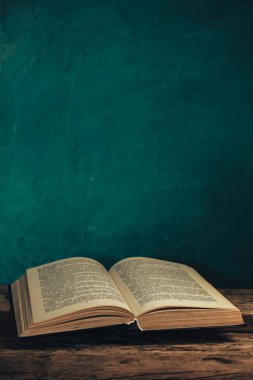 Eski meşe ağacından bir masada eski bir kitap ve arkasında yeşil bir duvar var..