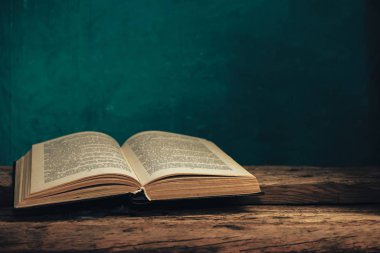 Eski meşe ağacından bir masada eski bir kitap ve arkasında yeşil bir duvar var..