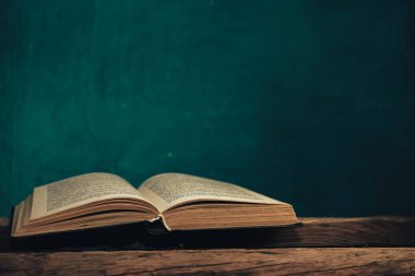 Eski meşe ağacından bir masada eski bir kitap ve arkasında yeşil bir duvar var..