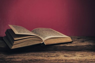 Eski meşe ağacından bir masanın üzerinde eski bir kitap ve arkasında kırmızı bir duvar var..