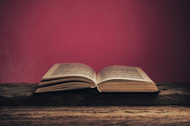 Eski meşe ağacından bir masanın üzerinde eski bir kitap ve arkasında kırmızı bir duvar var..