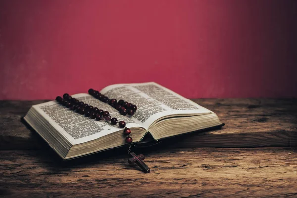 打开圣经和珠子钉在老橡木桌子上 美丽的红墙背景 — 图库照片