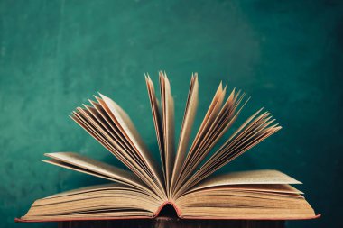 Eski ahşap bir masa üzerinde eski açık kitap ve arkasında yeşil duvar arka planı.