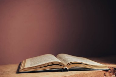 Güzel, açık, antika bir kitap. Tasarım için model arka planı. Kırmızı ahşap masa ve kırmızı duvar arkaplanındaki kitap..
