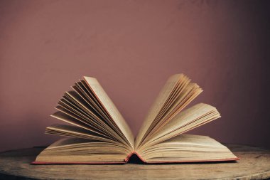 Açık antika bir kitap. Tasarım için model arka planı. Yuvarlak ahşap masa ve kırmızı duvar arkaplanındaki kitap..