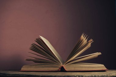 Açık antika bir kitap. Tasarım için model arka planı. Yuvarlak ahşap masa ve kırmızı duvar arkaplanındaki kitap..