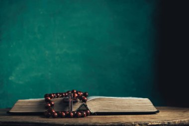 Eski yuvarlak ahşap bir masanın üzerinde kutsal İncil ve boncuklar aç. Güzel yeşil duvar arkaplanı.