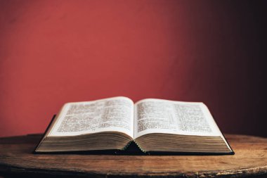 Eski, kahverengi, yuvarlak, tahta bir masanın üzerinde Kutsal Kitap 'ı aç. Güzel kırmızı duvar arkaplanı.