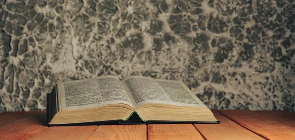 Open bible on a red old wooden table. Beautiful gray white wall background.