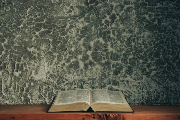 Open bible on a brown old wooden table. Beautiful gray white wall background.