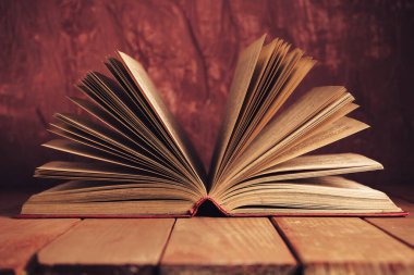 Kırmızı ahşap bir masada eski güzel bir kitap ve arkasında koyu kırmızı bir duvar var..