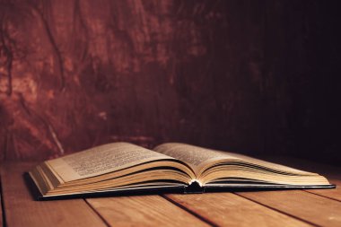 Kırmızı ahşap bir masada eski güzel bir kitap ve arkasında koyu kırmızı bir duvar var..