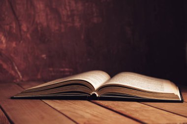 Kırmızı ahşap bir masada eski güzel bir kitap ve arkasında koyu kırmızı bir duvar var..