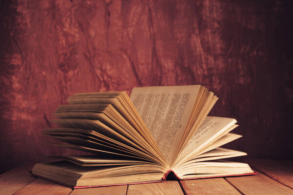 Beautiful ancient open old book on a red wooden table and dark-red wall background behind.