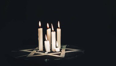 Altı yanan mum ve Davut Yıldızı siyah bir arkaplanda.