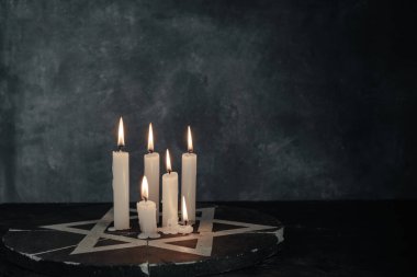 Altı yanan mum ve Davut Yıldızı koyu gri arka plan duvarına karşı.