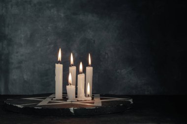 Altı yanan mum ve Davut Yıldızı koyu gri arka plan duvarına karşı.