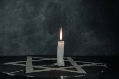 Bir yanan mumla Davut Yıldızı 'nı koyu gri arka plan duvarına yaklaştır..