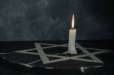 Bir yanan mumla Davut Yıldızı 'nı koyu gri arka plan duvarına yaklaştır..