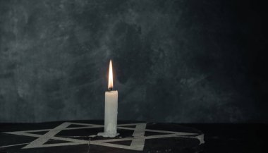 Bir yanan mumla Davut Yıldızı 'nı koyu gri arka plan duvarına yaklaştır..