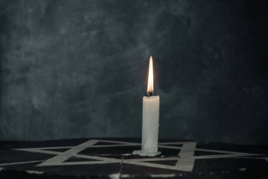 Bir yanan mumla Davut Yıldızı 'nı koyu gri arka plan duvarına yaklaştır..