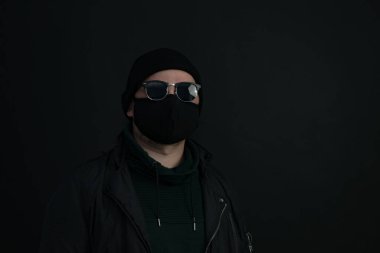 Yüz maskesi takan genç bir adam. Siyah şapkalı yakışıklı adam siyah tıbbi maske takıyor, gri arka plan, fotokopi alanı. Salgın koronavirüs covid-19 karantina dönemi konsepti