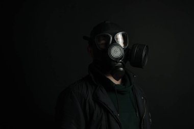 Yüz gazı maskesi takan genç bir adam. Yakışıklı adam siyah tıbbi maske takıyor, siyah arka plan, fotokopi alanı. Salgın koronavirüs covid-19 karantina dönemi konsepti.