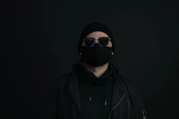 Young man wearing face mask. Handsome man in black hat wear black medical mask, gray background, copy space. Pandemic coronavirus covid-19 quarantine period concept