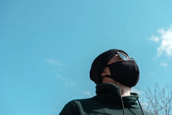 Young man wearing face mask. Handsome man in sunglasses wear black medical mask, sky background, copy space. Pandemic coronavirus covid-19 quarantine period concept