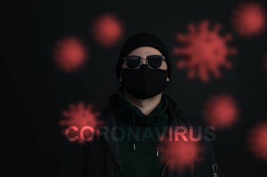Yüz maskesi takan genç bir adam. Siyah şapkalı yakışıklı adam siyah tıbbi maske takıyor, gri arka plan, fotokopi alanı. Salgın koronavirüs covid-19 karantina dönemi konsepti