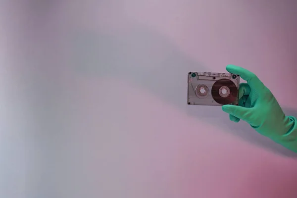 Green Hand holding audio cassette tape in the color light. Beautiful minimal in neon light. Minimalism retro style concept. Background pattern for design.