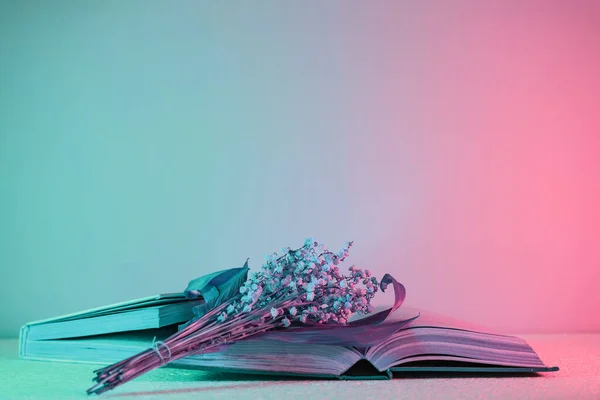 Close up Beautiful open book and flowers  in neon light. Minimalism retro style concept. 80s. Background pattern for design.