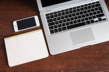 Not Defteri, dizüstü bilgisayar ve ahşap masa üstünde hareket eden telefon