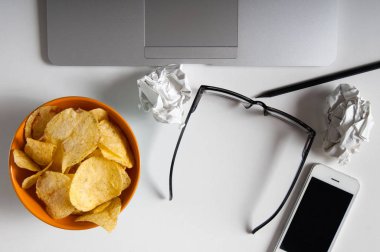 Dizüstü bilgisayar, buruşuk kağıt ve ahşap masa üzerindeki fişlere kase çalışma alanı. Kötü alışkanlıkları kavramı