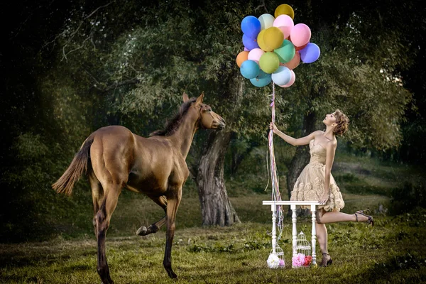 Sanat fotoğrafı fairytale ormandaki açık. Harika elbise inanılmaz ince atı ile çayır üzerinde renkli balonlar ile gülümseyerek poz şirin kısa Kahverengi kıvırcık saçlı güzel ince model kadın