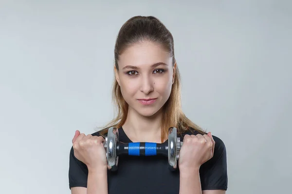 Mükemmel bir siyah t shirt esmer saçlı genç güzel seksi kadın fotoğraf Studio gri arka plan üzerinde metal dumbbell ile poz. Fitness spor sağlık sağlık modeli portre fotoğraf çekim