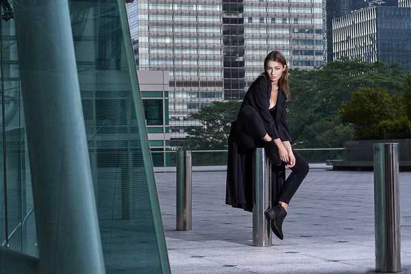 Uzun siyah bir ceket, Hong Kong sokakta mimari camlar yakın poz rahat tarzı mükemmel esmer saçlı güzel genç seksi kadın. Moda sokak vogue modeli açık fotoğraf çekim