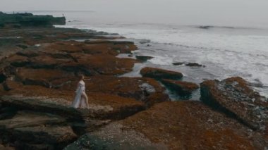 Uzun seksi elbiseli güzel ince genç erkek hava görüntüleri üzerinde okyanus plaj buzlu günbatımında video 4 k uçak yukarıdan çekim harika manzara, muhteşem model teşkil duruyor