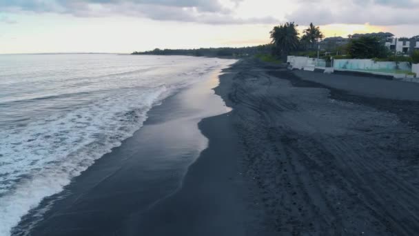 美丽快乐的年轻女性在牛仔裤短裤和一个灰色的 T恤海滩上的黑色沙滩和海浪在巴厘岛日落 拍摄视频4K 从上面的飞机 美妙的景色 令人惊叹的模型构成 — 图库视频影像